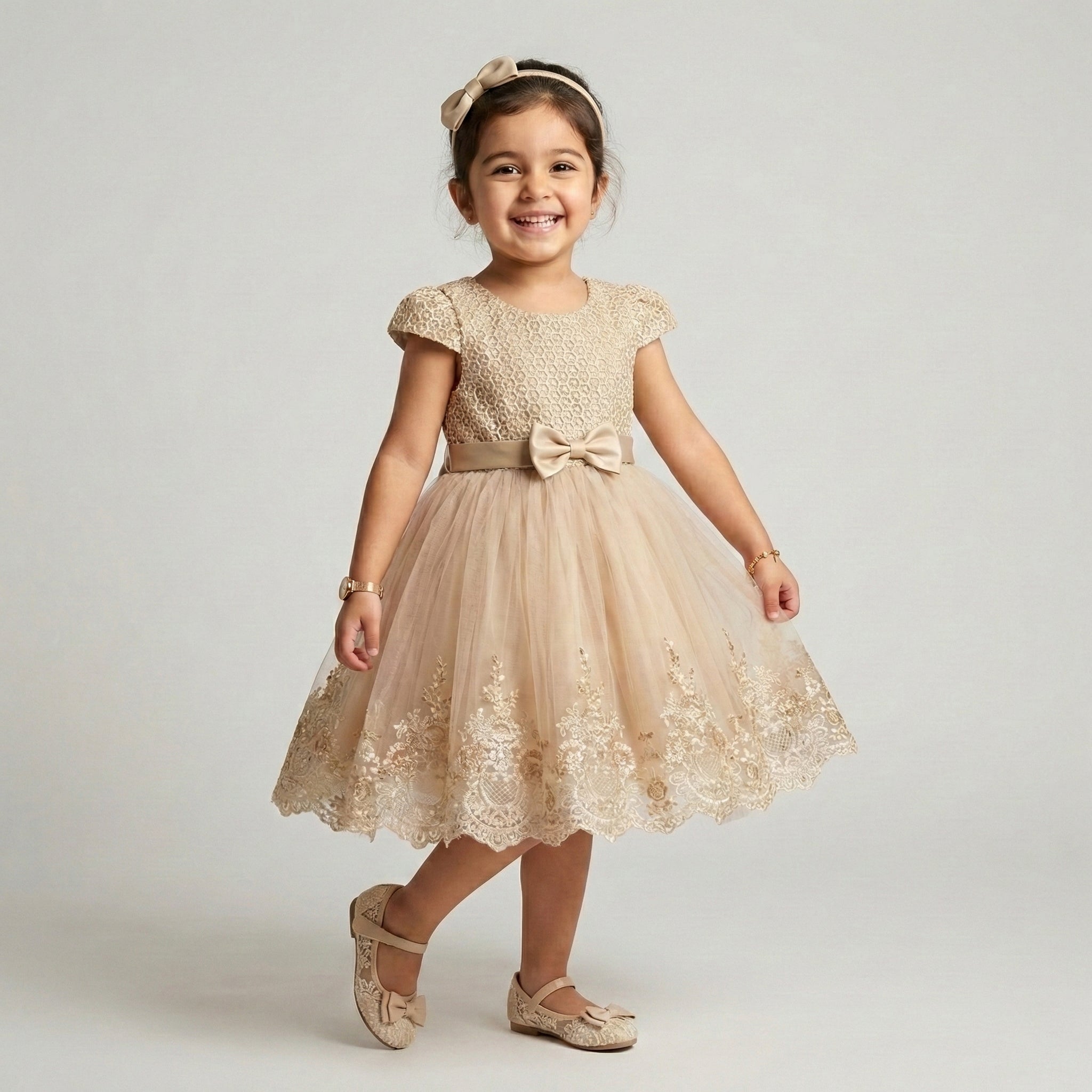 Young girl wearing a beige lace dress with a bow on a plain background